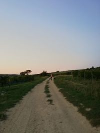 Dirt road amidst field against clear sky