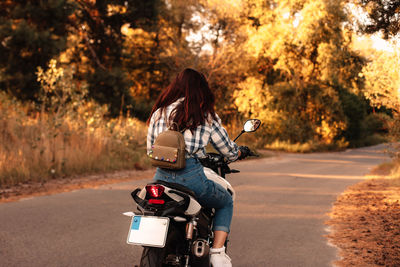 Rear view of woman riding motorcycle on road