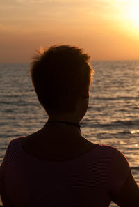 Rear view of man looking at sea against sunset sky