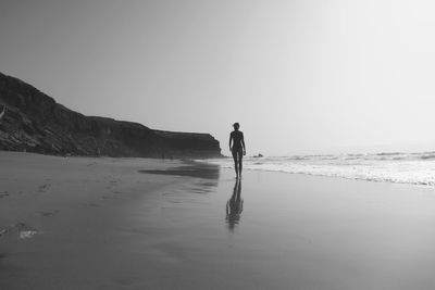 Rear view of man walking at beach against clear sky