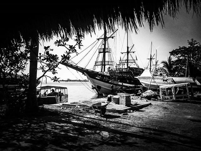 nautical vessel, moored, boat, tree, water, palm tree, transportation, mode of transport, sea, chair, sunlight, sky, absence, built structure, outdoors, table, day, nature, clear sky, mast