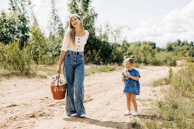 Happy mother and daughter are walking along a country road with a wicker basket in their hands