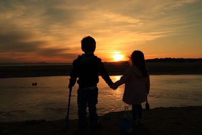 Two children standing on beach at sunset