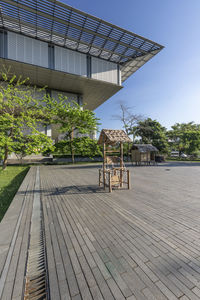 Empty chairs on footpath by building against sky