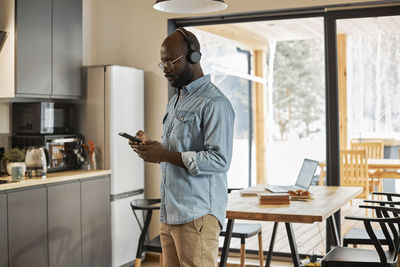 Man using smart phone standing in kitchen at home