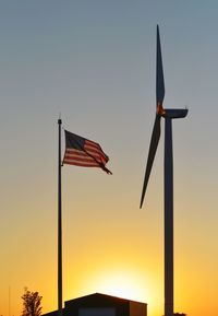 Low angle view of american flag by windmill during sunset