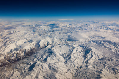 Aerial view of snowcapped mountains against blue sky