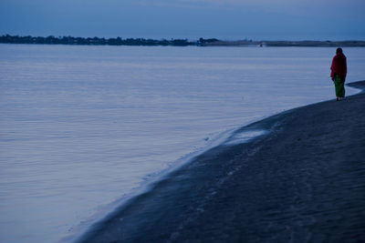 Rear view of woman walking on beach against sky