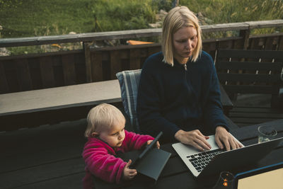 Mother using laptop while daughter holding digital tablet at table in holiday villa