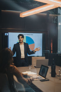 Young businessman gesturing while giving presentation to female colleague in board room