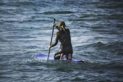 Rear view of woman paddleboarding in sea