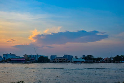 Buildings by sea against sky during sunset