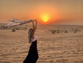Rear view of woman standing at beach against sky during sunset