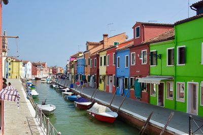 Boats moored in canal by buildings against sky