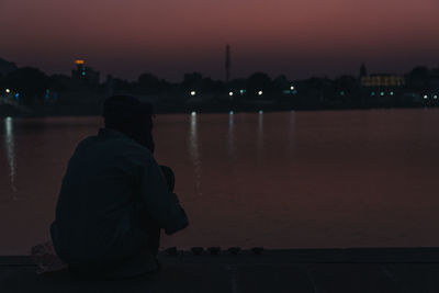 Rear view of woman looking at river against sky at night