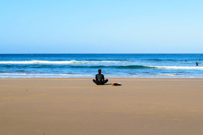 Man sitting on beach against clear sky