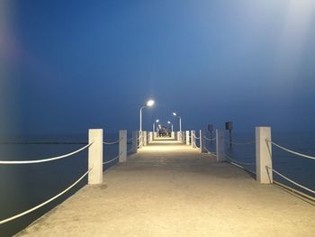 Illuminated street lights by sea against clear sky at night