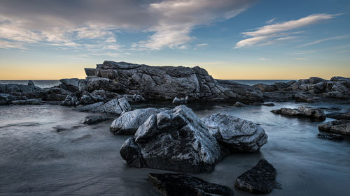 Rocks in sea against sky during sunset