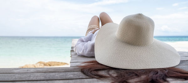 Rear view of woman wearing hat standing by sea against sky