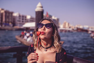 Close-up of young woman puckering while holding heart shaped object against lake
