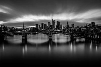 Bridge over river by buildings in city against sky in frankfurt, germany 