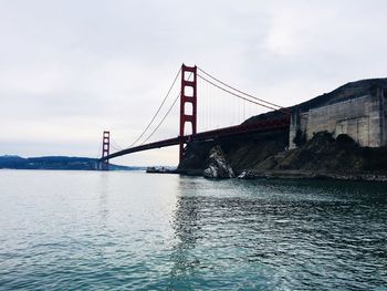 Low angle view of golden gate bridge over sea against cloudy sky