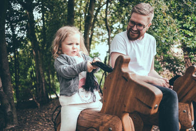 Full length of father and daughter sitting on tree