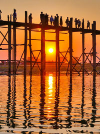 Silhouette people standing by bridge against sky during sunset