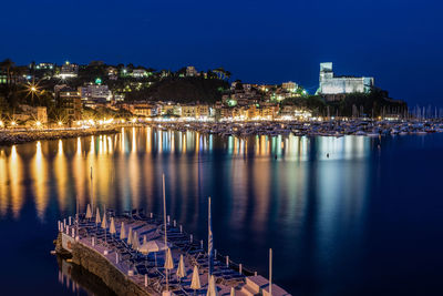 Illuminated buildings by river against sky at night