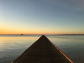 Pier over sea against clear sky during sunset