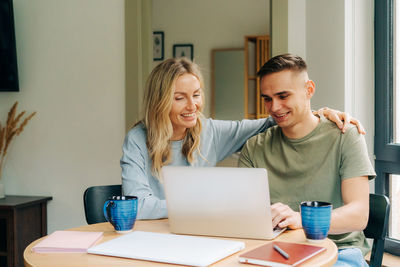 Young smiling woman and man sitting home, drinking coffee and watching a movie on a computer.