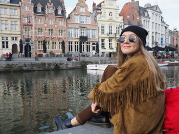 Young woman wearing sunglasses at canal against buildings