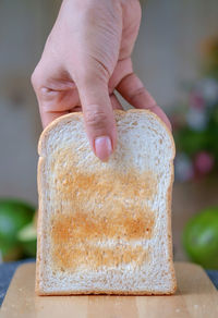 Cropped image of hand holding toasted bread on cutting board