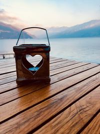 Tea light in lantern on pier over lake against sky