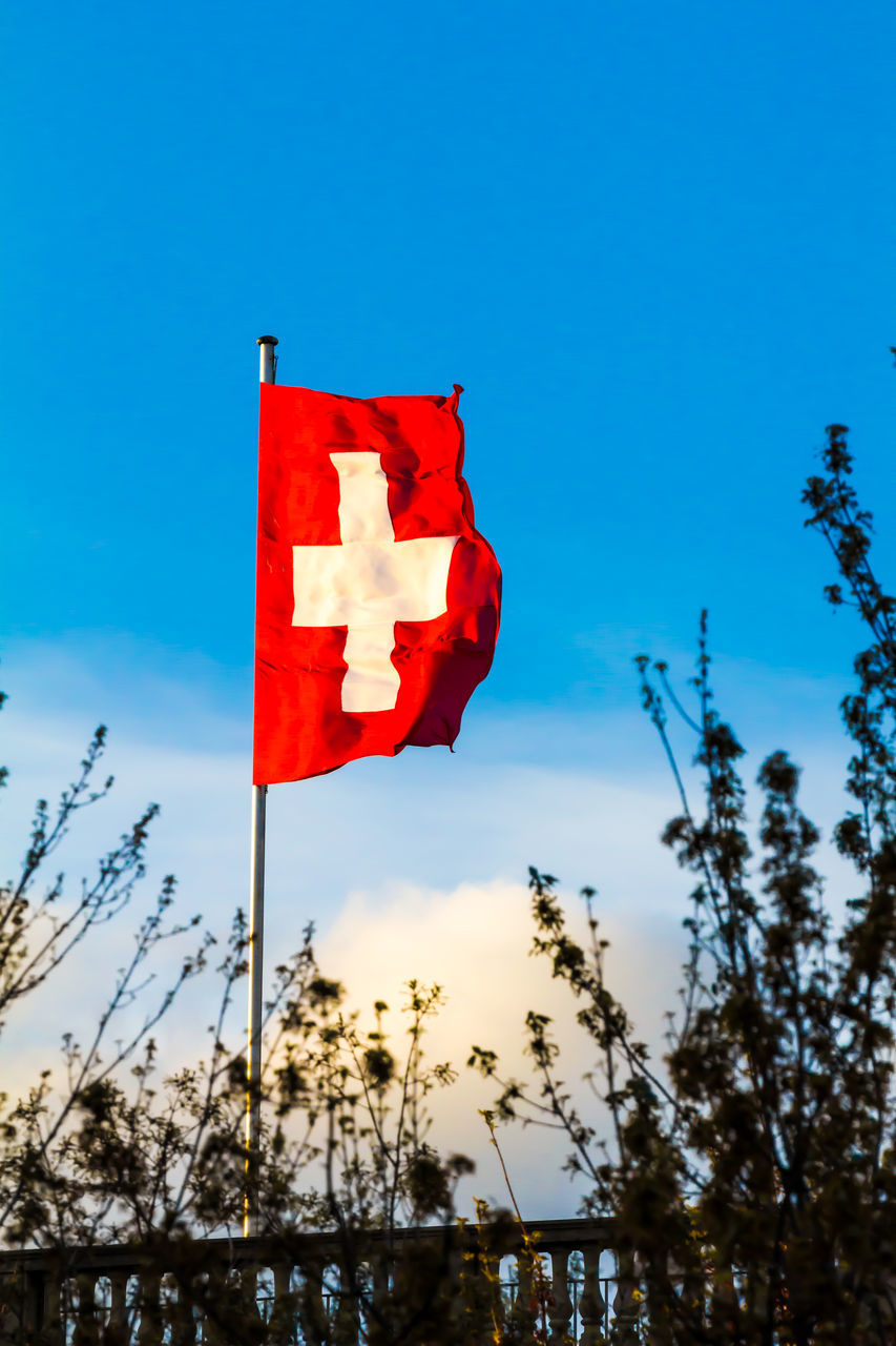 LOW ANGLE VIEW OF RED FLAG ON BLUE SKY