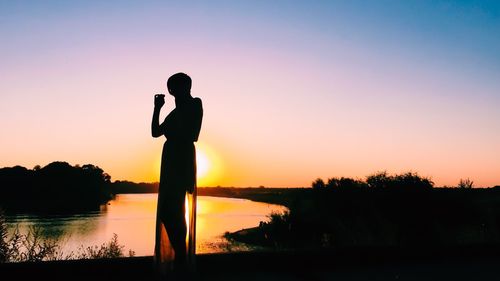 Silhouette woman standing by lake against sky during sunset