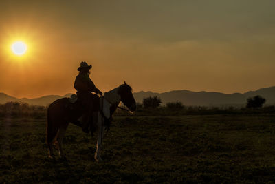 Horse riding horses on field against sky during sunset