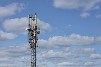 Cellular antennas on a metal mast against a blue cloudy sky.