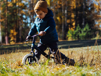 Cute toddler boy in casual clothes riding on balance bike in autumn forest