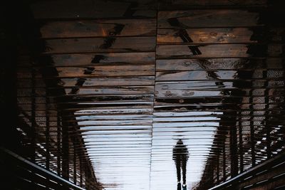Reflection of a man walking on a wooden bridge 