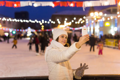 Full length portrait of woman photographing illuminated city