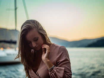 Portrait of young woman looking at lake against sky