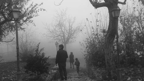 People walking by bare trees against sky