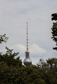 Trees by fernsehturm against cloudy sky