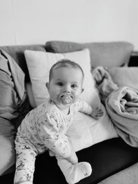 Portrait of cute baby girl sucking pacifier while sitting on sofa at home