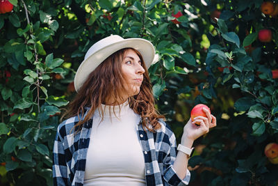 Woman in a hat holding ripe red apple from the tree. autumn harvest