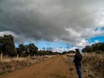 Rear view of man on road amidst field against sky