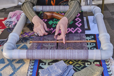 Hands of senior woman weaves carpet with traditional asian pattern on handloom at crafts fair