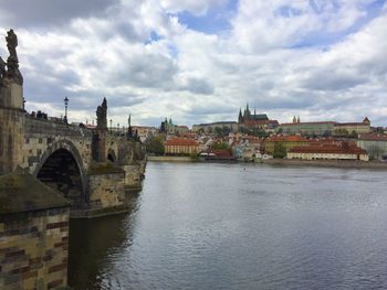 Arch bridge over river by buildings against sky