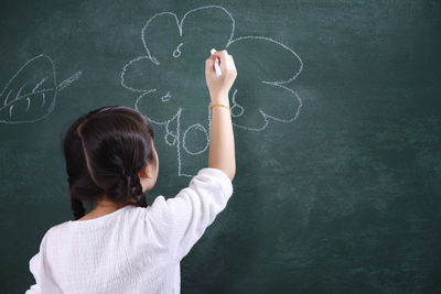 Rear view of girl drawing on blackboard